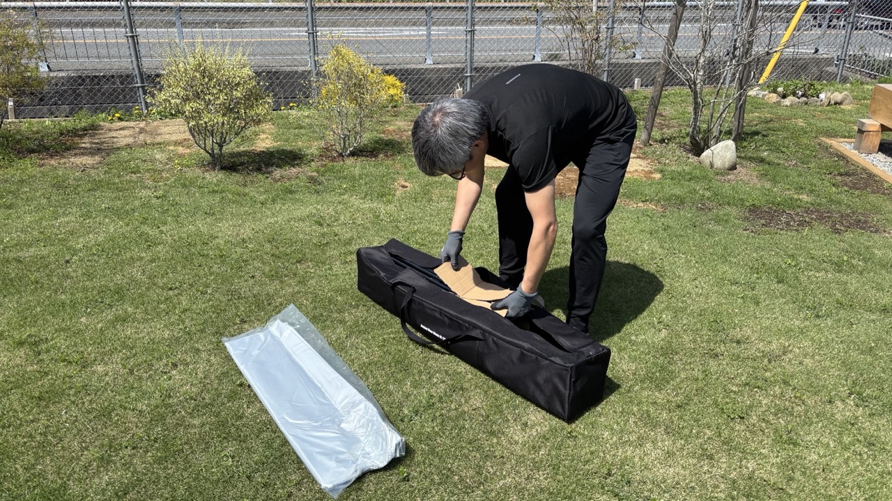芝生の上でワンタッチタープを取り出す男性