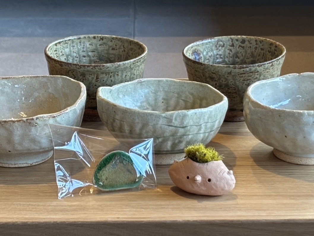 手作りの茶碗と購入した食器、ブローチ、鉢植えが並んでいる